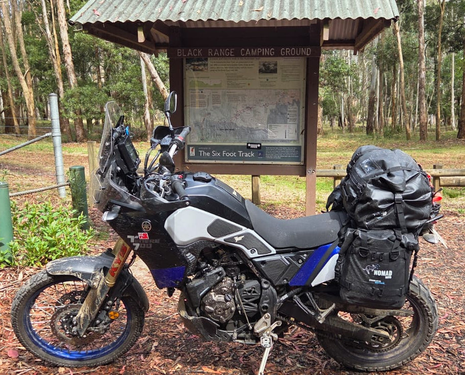 Nomad Moto Motorcycle with luggage at a camping area in a forest